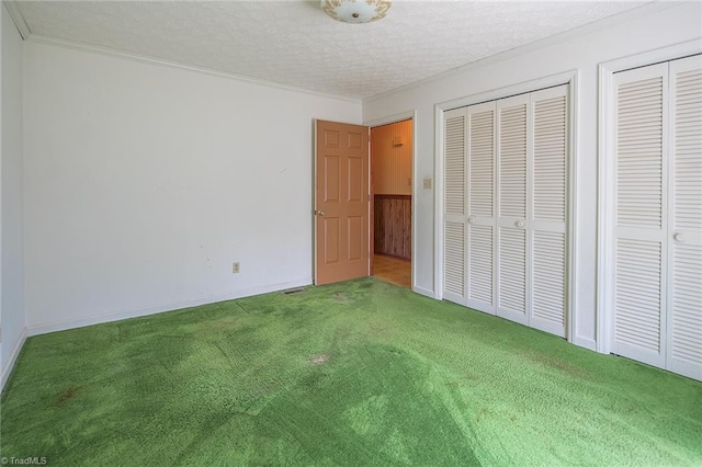 unfurnished bedroom featuring carpet, wood walls, two closets, ornamental molding, and a textured ceiling