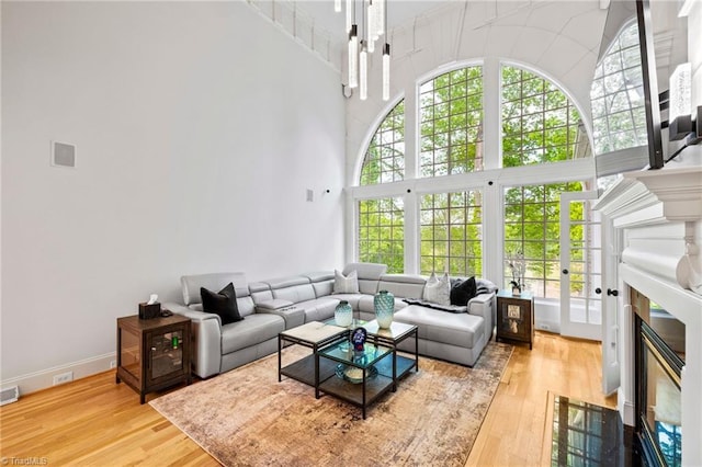 living room with wood finished floors, high vaulted ceiling, a fireplace with flush hearth, and baseboards