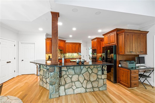 kitchen with decorative columns, black appliances, dark countertops, crown molding, and light wood-type flooring