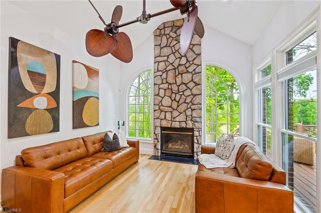 living area with wood finished floors, a stone fireplace, and high vaulted ceiling