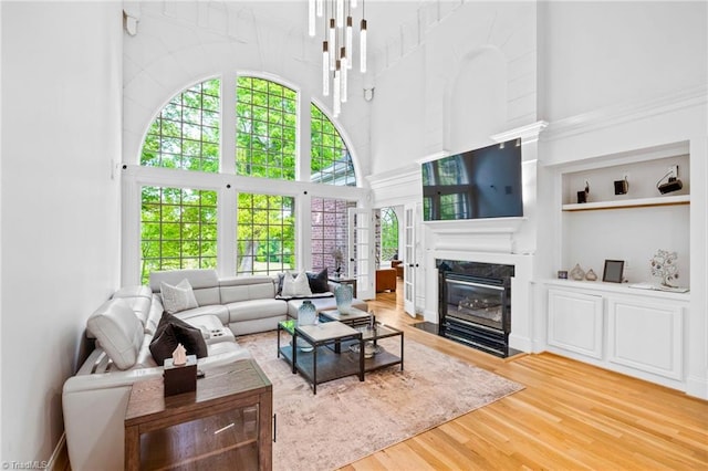 living area with a towering ceiling, wood finished floors, a fireplace, and built in features