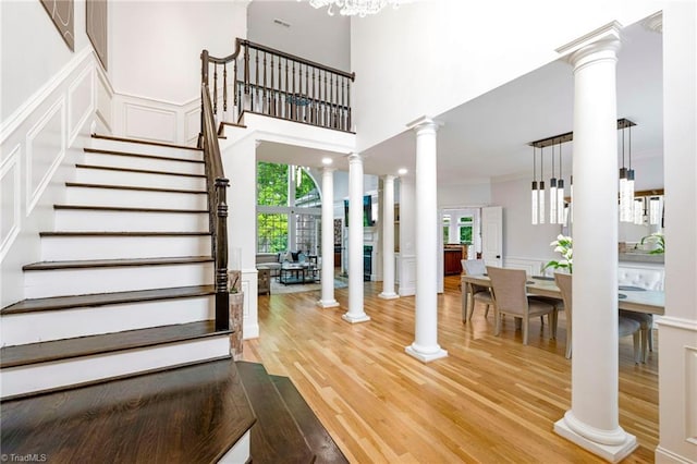 stairs featuring ornate columns, wood finished floors, a decorative wall, ornamental molding, and a chandelier