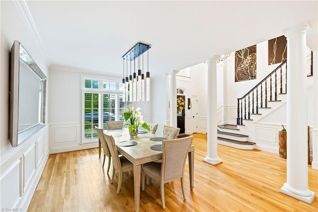 dining space with decorative columns, a decorative wall, crown molding, light wood finished floors, and stairs