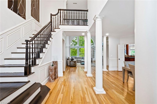 entrance foyer featuring a decorative wall, decorative columns, light wood finished floors, ornamental molding, and wainscoting