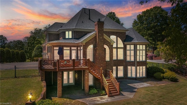 back of property at dusk with brick siding, a deck, a chimney, stairway, and a shingled roof