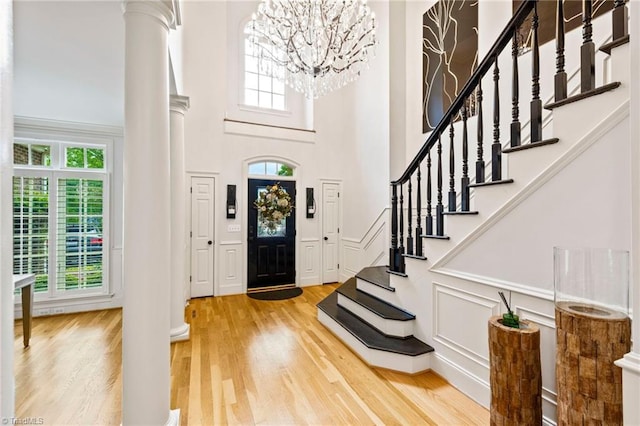 entrance foyer featuring decorative columns, a high ceiling, a chandelier, light wood-style flooring, and stairs