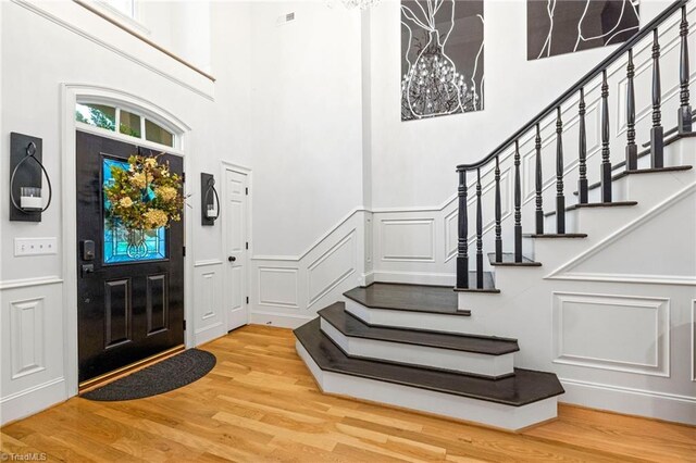 foyer featuring a decorative wall, stairs, a high ceiling, wood finished floors, and a wainscoted wall