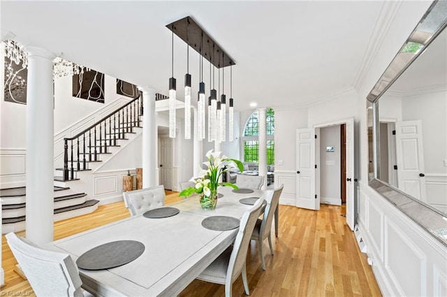 dining room with a decorative wall, light wood finished floors, crown molding, stairway, and a wainscoted wall
