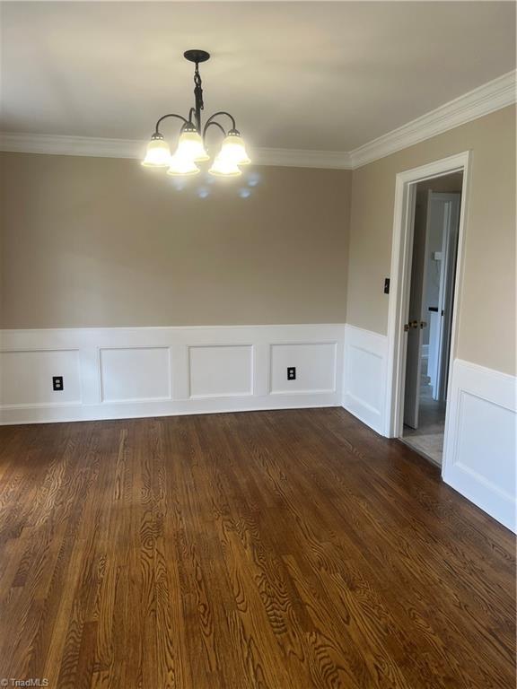 empty room featuring a chandelier, dark wood finished floors, and ornamental molding