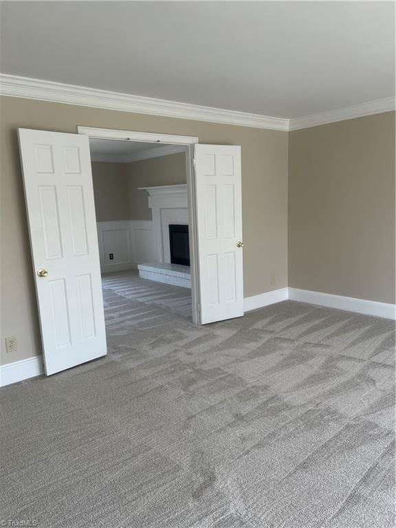 unfurnished room with carpet flooring, a fireplace, baseboards, and ornamental molding