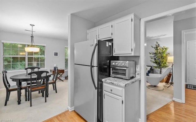 kitchen featuring stainless steel refrigerator, white cabinetry, decorative light fixtures, and light hardwood / wood-style flooring