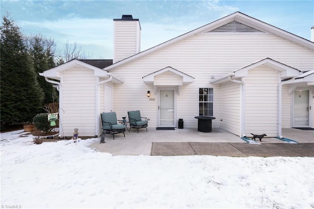 snow covered rear of property with a patio area