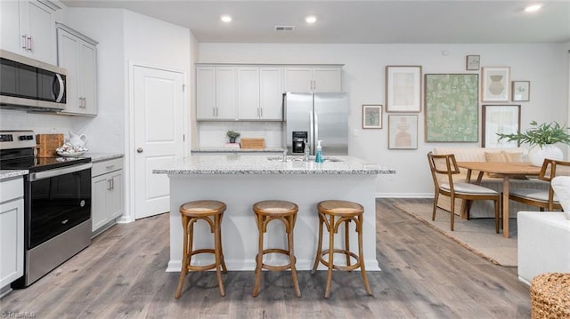 1436 Amberview Ln, Kernersville, NC 27284 - kitchen with appliances with stainless steel finishes, backsplash, an island with sink, wood finished floors, and light stone counters