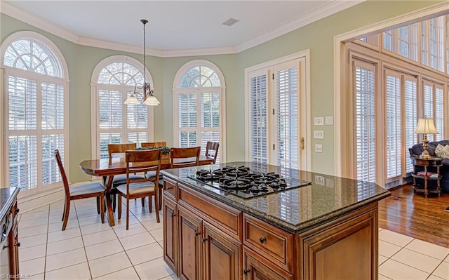 kitchen with light hardwood / wood-style floors, gas stovetop, dark stone countertops, a center island, and ornamental molding