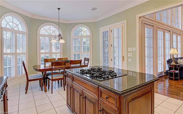 kitchen with stainless steel gas stovetop, ornamental molding, dark stone countertops, light tile patterned flooring, and pendant lighting