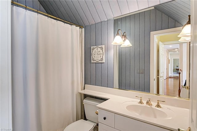 bathroom featuring toilet, vanity, wood walls, and lofted ceiling