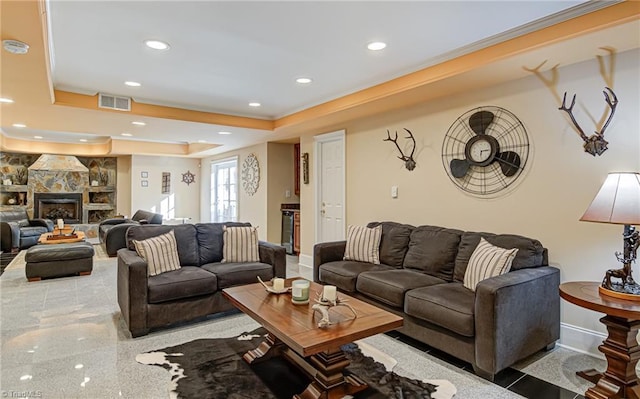 living room featuring ornamental molding, a stone fireplace, and a raised ceiling