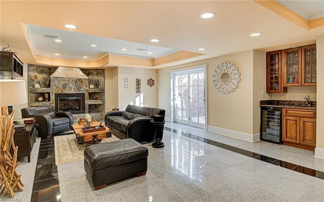 living room featuring a tray ceiling, crown molding, wine cooler, and a stone fireplace