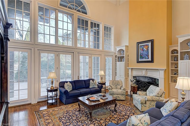 living room with a high end fireplace, built in shelves, wood-type flooring, and a towering ceiling