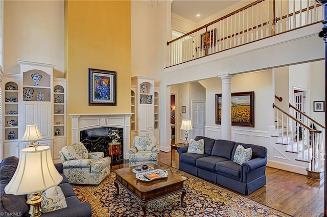 living room with a premium fireplace, decorative columns, hardwood / wood-style flooring, ornamental molding, and a towering ceiling