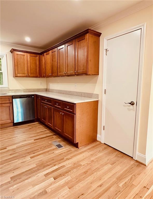 5670 Plantation Dr, Winston-Salem, NC 27105 - kitchen featuring stainless steel dishwasher, crown molding, light countertops, light wood-type flooring, and brown cabinets