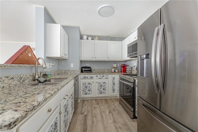 kitchen with sink, light hardwood / wood-style flooring, appliances with stainless steel finishes, light stone countertops, and white cabinets