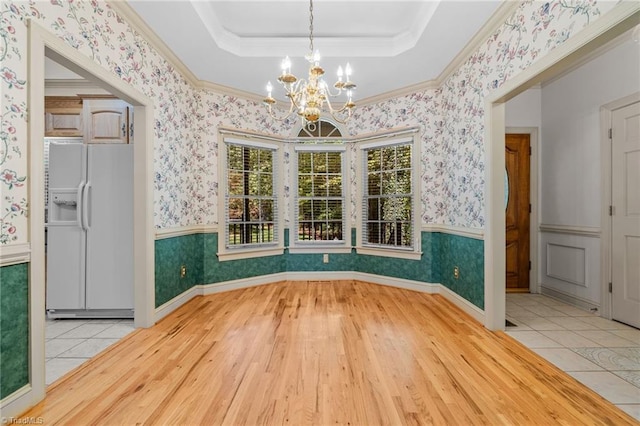 unfurnished dining area featuring a notable chandelier, ornamental molding, a raised ceiling, and light wood-type flooring