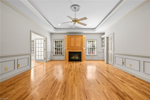 unfurnished living room with ornamental molding, a tray ceiling, light hardwood / wood-style floors, and ceiling fan