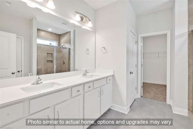 bathroom with a walk in closet, double vanity, a stall shower, and a sink