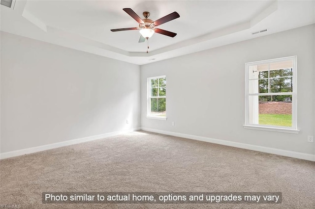 carpeted empty room featuring a tray ceiling, baseboards, visible vents, and a ceiling fan