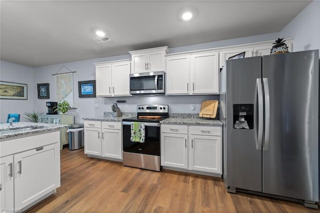 kitchen with appliances with stainless steel finishes, light stone countertops, white cabinets, and wood finished floors