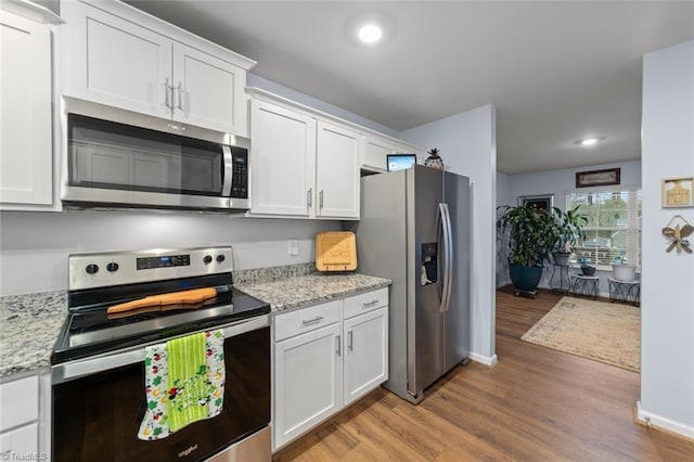 kitchen with light wood finished floors, stainless steel appliances, white cabinetry, light stone countertops, and baseboards