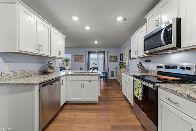 kitchen featuring stainless steel appliances, white cabinetry, a sink, wood finished floors, and a peninsula