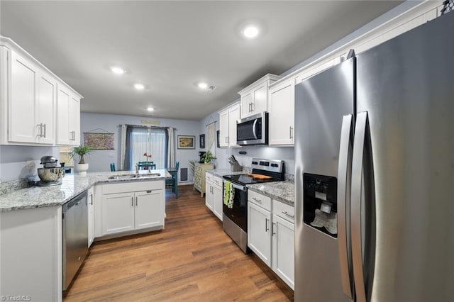 kitchen with stainless steel appliances, a peninsula, wood finished floors, a sink, and white cabinetry