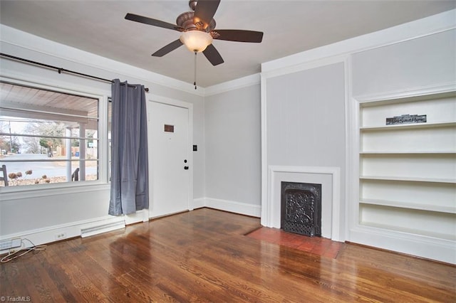 unfurnished living room featuring dark hardwood / wood-style flooring, built in shelves, crown molding, and ceiling fan