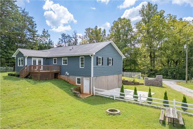 back of house with a wooden deck, a lawn, and a fire pit