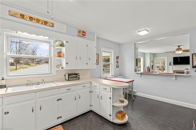 kitchen with a peninsula, a sink, white cabinets, light countertops, and open shelves