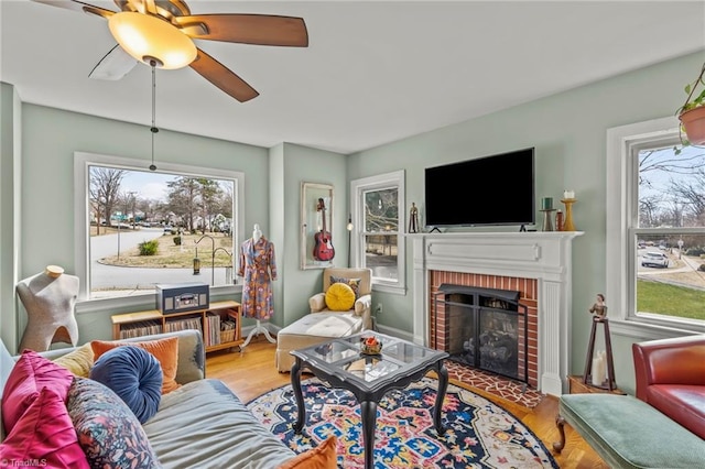 living area with a brick fireplace, ceiling fan, and wood finished floors