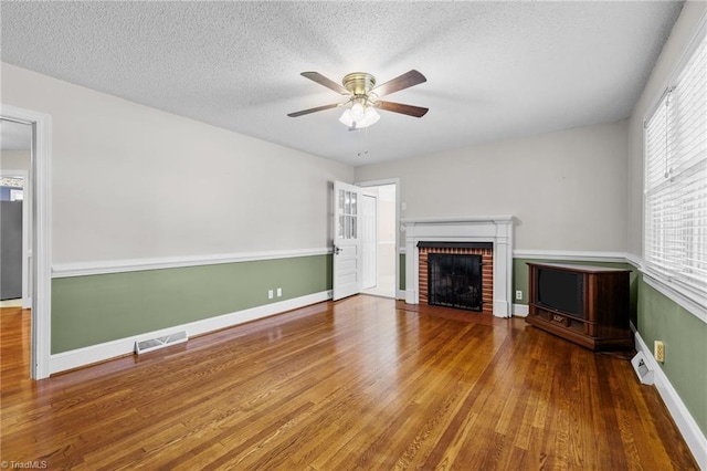 unfurnished living room with ceiling fan, wood-type flooring, a textured ceiling, and a brick fireplace