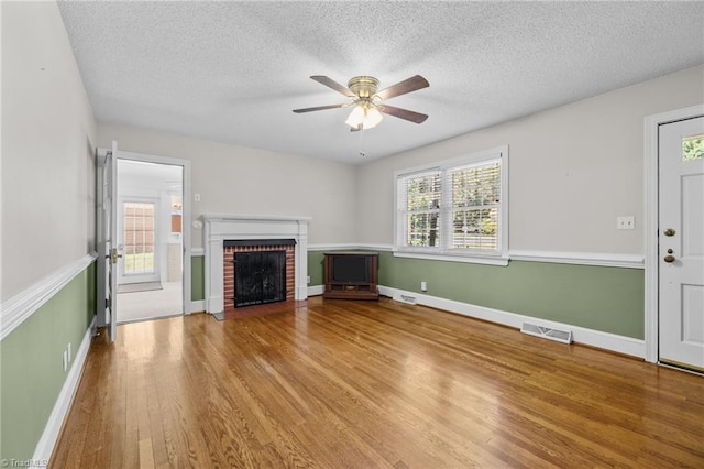 unfurnished living room with hardwood / wood-style flooring, a brick fireplace, plenty of natural light, and ceiling fan