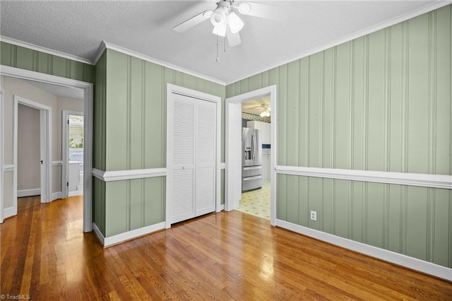 unfurnished bedroom with hardwood / wood-style flooring, ceiling fan, ornamental molding, stainless steel fridge with ice dispenser, and a closet