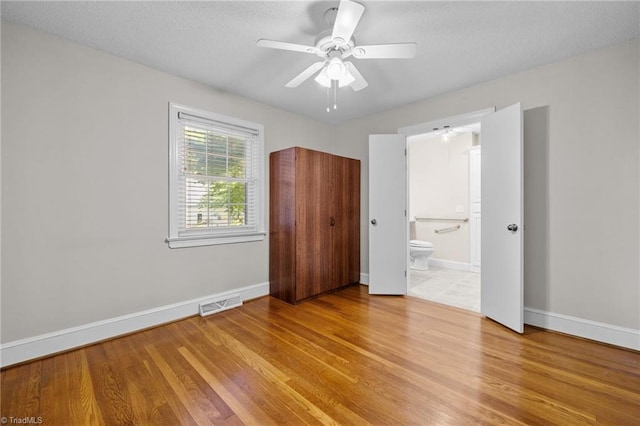 unfurnished bedroom featuring wood-type flooring, a textured ceiling, ensuite bathroom, and ceiling fan