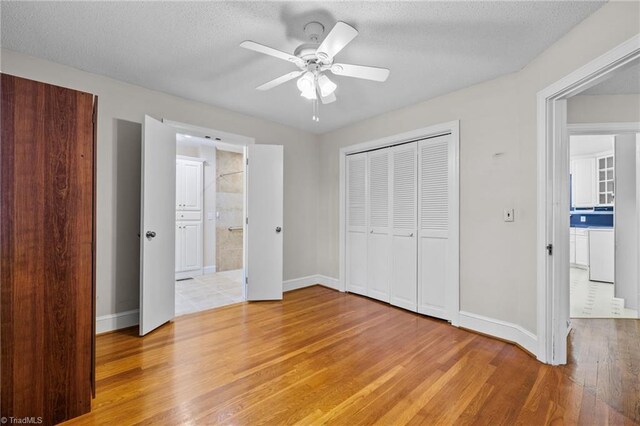 unfurnished bedroom with a textured ceiling, light wood-type flooring, ensuite bath, and ceiling fan