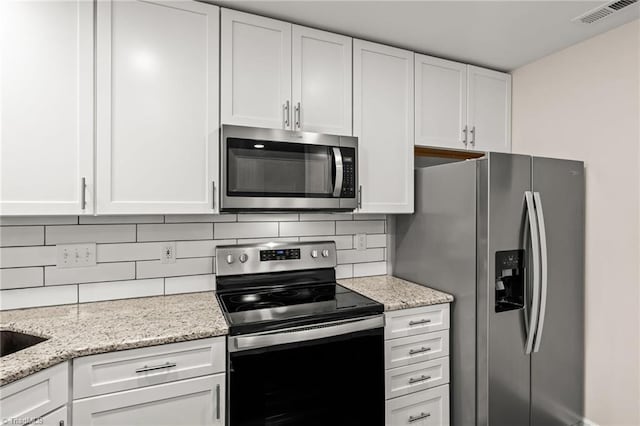 kitchen with tasteful backsplash, white cabinets, and appliances with stainless steel finishes