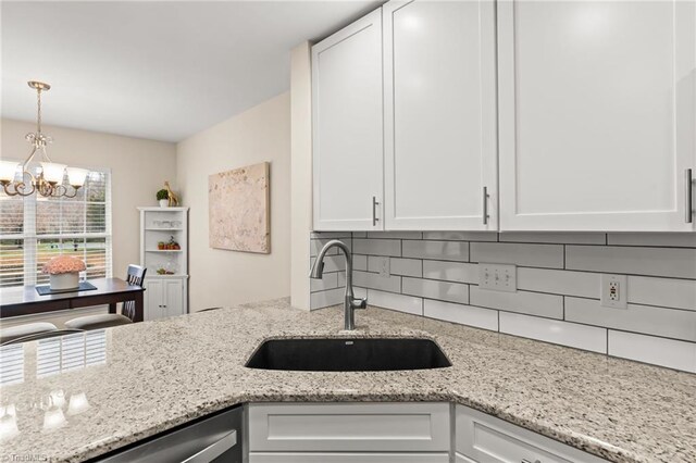 kitchen featuring white cabinets, backsplash, an inviting chandelier, and sink