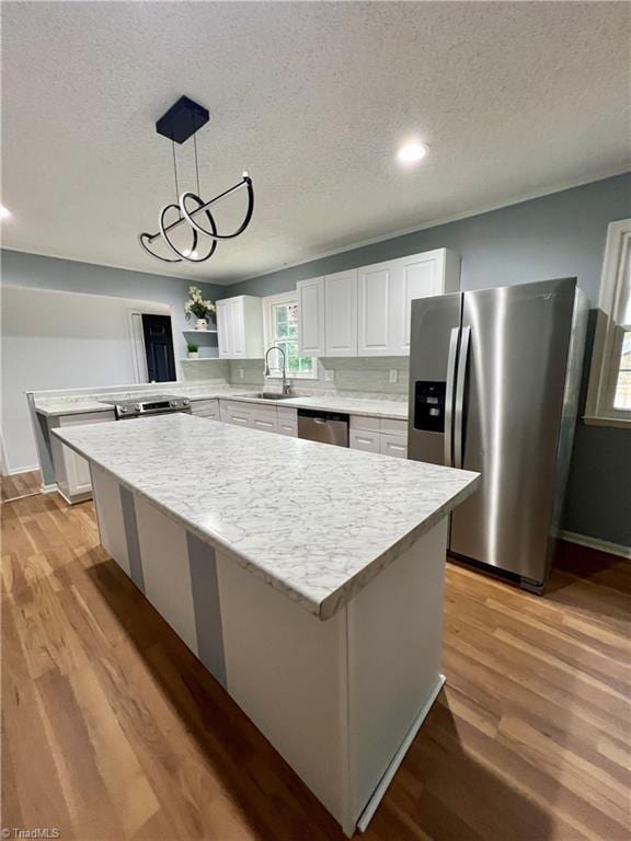 kitchen with a center island, light wood-style flooring, stainless steel appliances, white cabinetry, and a sink