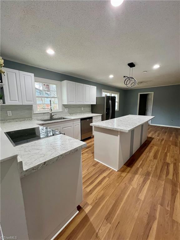 kitchen featuring freestanding refrigerator, a sink, light wood-style floors, stainless steel dishwasher, and black electric stovetop