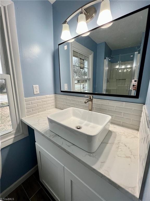 full bathroom with backsplash, a shower stall, baseboards, marble finish floor, and vanity