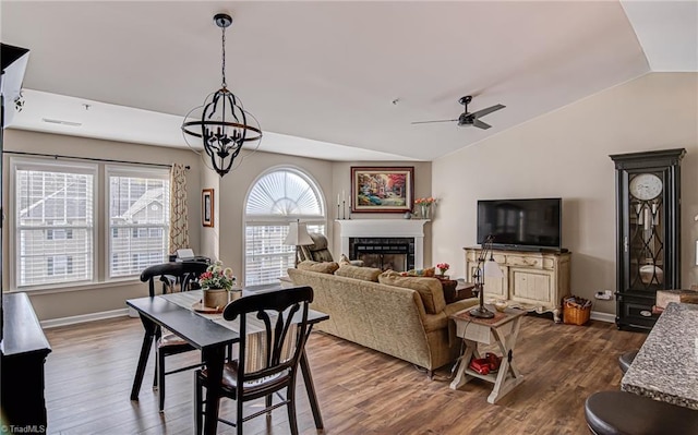 dining space featuring ceiling fan with notable chandelier, dark wood-type flooring, and lofted ceiling