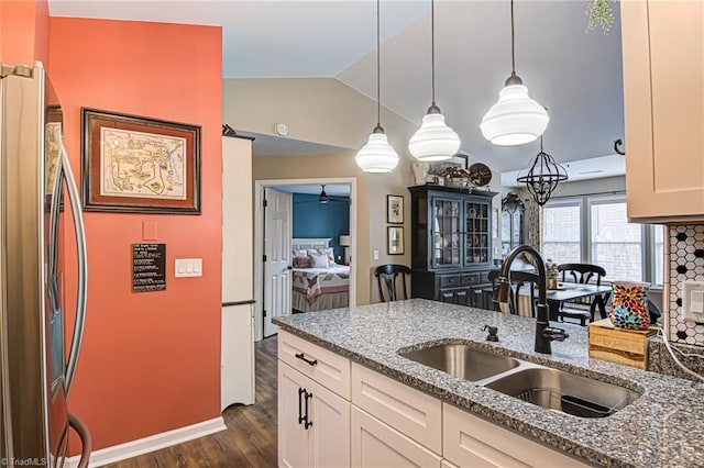 kitchen featuring sink, dark wood-type flooring, light stone counters, stainless steel fridge, and pendant lighting